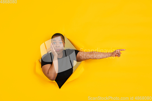 Image of Cheerful young woman poses in torn yellow paper hole background, emotional and expressive