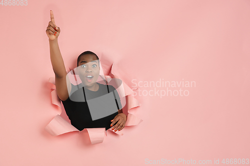 Image of Cheerful young woman poses in torn coral paper hole background, emotional and expressive