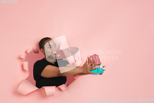 Image of Cheerful young woman poses in torn coral paper hole background, emotional and expressive