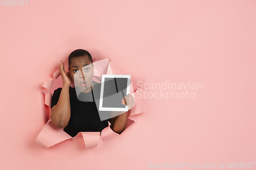 Image of Cheerful young woman poses in torn coral paper hole background, emotional and expressive