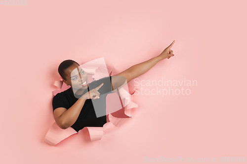 Image of Cheerful young woman poses in torn coral paper hole background, emotional and expressive