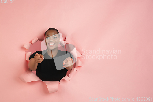 Image of Cheerful young woman poses in torn coral paper hole background, emotional and expressive