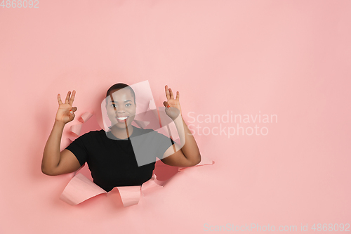 Image of Cheerful young woman poses in torn coral paper hole background, emotional and expressive