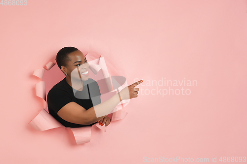 Image of Cheerful young woman poses in torn coral paper hole background, emotional and expressive