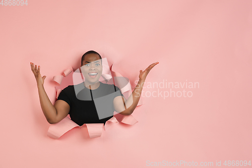 Image of Cheerful young woman poses in torn coral paper hole background, emotional and expressive