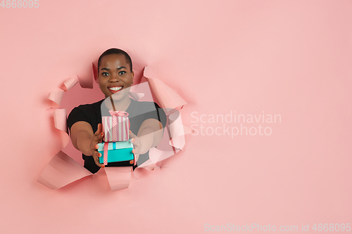 Image of Cheerful young woman poses in torn coral paper hole background, emotional and expressive