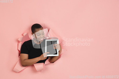 Image of Cheerful young woman poses in torn coral paper hole background, emotional and expressive