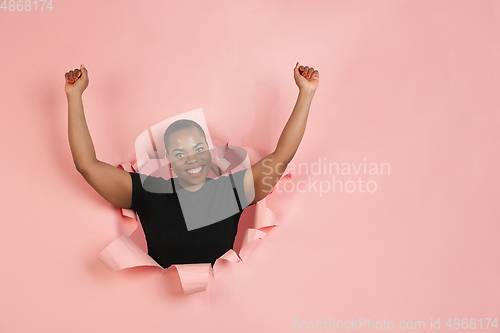 Image of Cheerful young woman poses in torn coral paper hole background, emotional and expressive