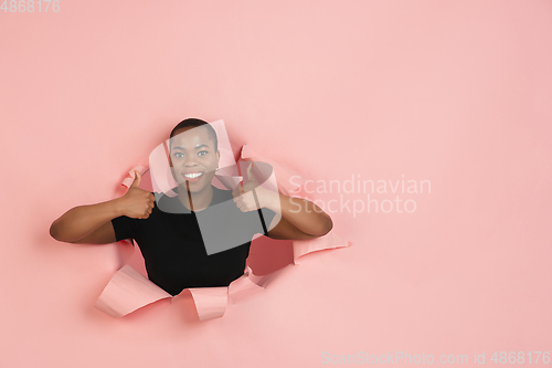 Image of Cheerful young woman poses in torn coral paper hole background, emotional and expressive