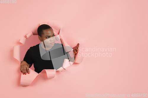 Image of Cheerful young woman poses in torn coral paper hole background, emotional and expressive