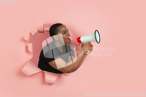 Image of Cheerful young woman poses in torn coral paper hole background, emotional and expressive, shouting with speaker