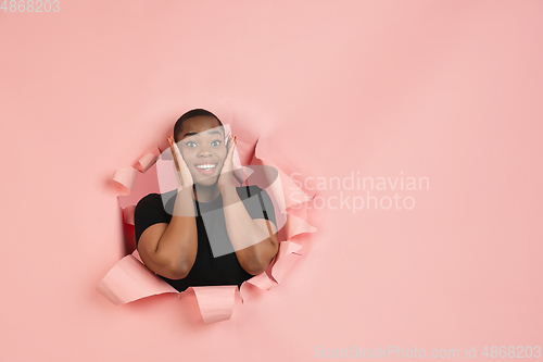 Image of Cheerful young woman poses in torn coral paper hole background, emotional and expressive