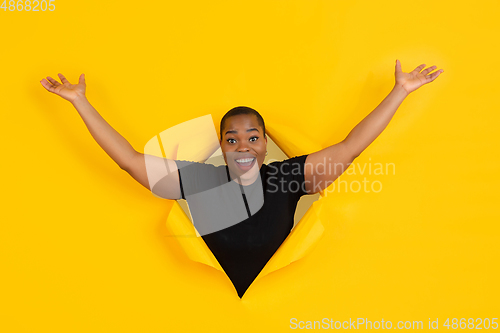 Image of Cheerful young woman poses in torn yellow paper hole background, emotional and expressive