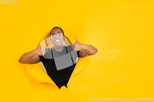 Image of Cheerful young woman poses in torn yellow paper hole background, emotional and expressive