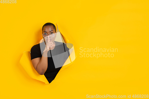 Image of Cheerful young woman poses in torn yellow paper hole background, emotional and expressive