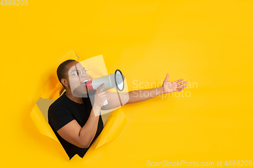 Image of Cheerful young woman poses in torn yellow paper hole background, emotional and expressive, shouting and calling with speaker