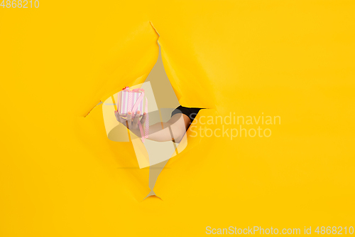 Image of Female hand giving gift in torn yellow paper hole background, celebration
