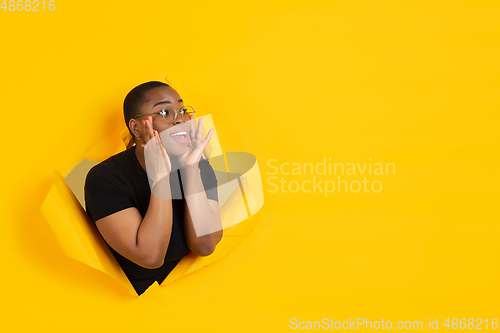 Image of Cheerful young woman poses in torn yellow paper hole background, emotional and expressive, shouting with speaker