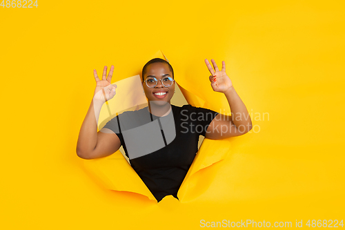 Image of Cheerful young woman poses in torn yellow paper hole background, emotional and expressive