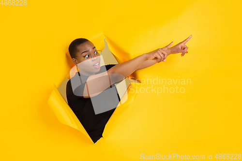 Image of Cheerful young woman poses in torn yellow paper hole background, emotional and expressive