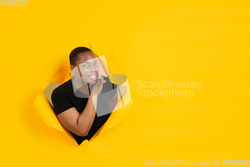 Image of Cheerful young woman poses in torn yellow paper hole background, emotional and expressive