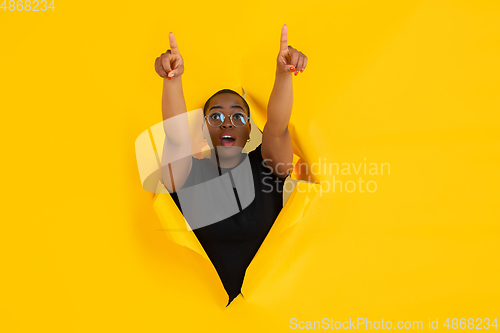 Image of Cheerful young woman poses in torn yellow paper hole background, emotional and expressive