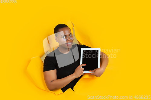 Image of Cheerful young woman poses in torn yellow paper hole background, emotional and expressive