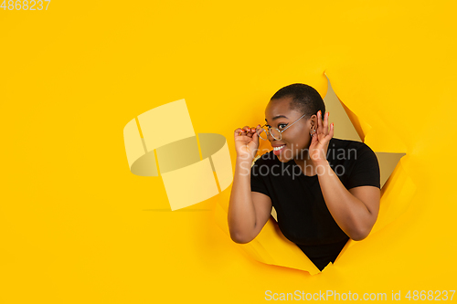 Image of Cheerful young woman poses in torn yellow paper hole background, emotional and expressive