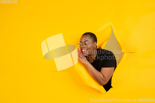 Image of Cheerful young woman poses in torn yellow paper hole background, emotional and expressive