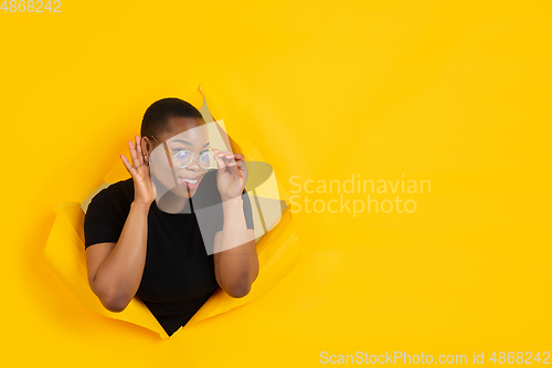 Image of Cheerful young woman poses in torn yellow paper hole background, emotional and expressive