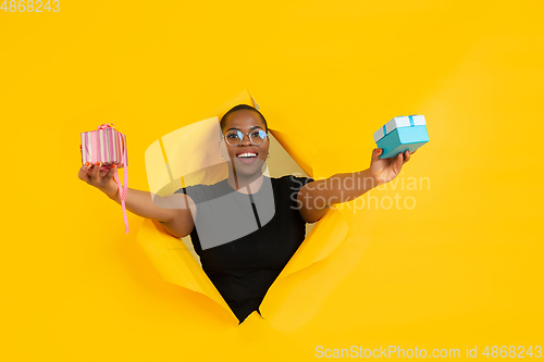 Image of Cheerful young woman poses in torn yellow paper hole background, emotional and expressive