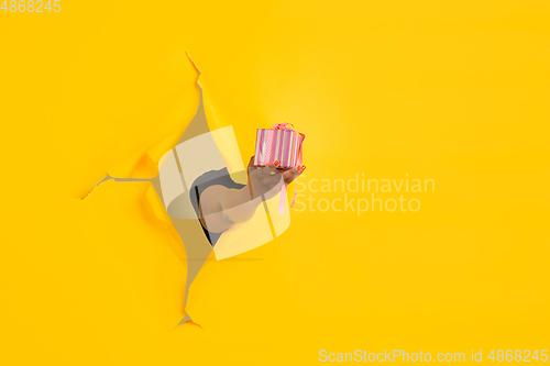 Image of Female hand giving gift in torn yellow paper hole background, celebration