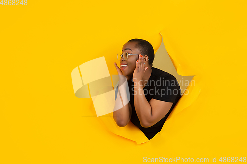 Image of Cheerful young woman poses in torn yellow paper hole background, emotional and expressive, shouting with speaker