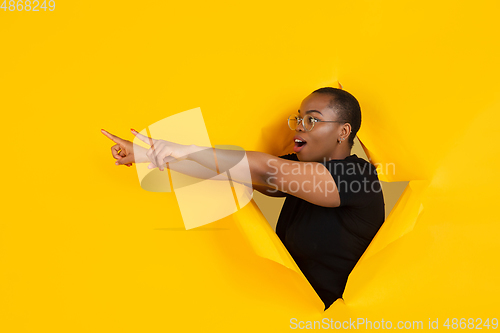 Image of Cheerful young woman poses in torn yellow paper hole background, emotional and expressive