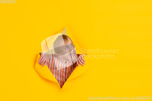 Image of Cheerful young man poses in torn yellow paper hole background, emotional and expressive