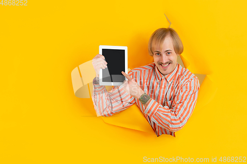 Image of Cheerful young man poses in torn yellow paper hole background, emotional and expressive