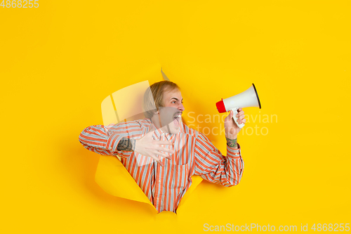 Image of Cheerful young man poses in torn yellow paper hole background, emotional and expressive