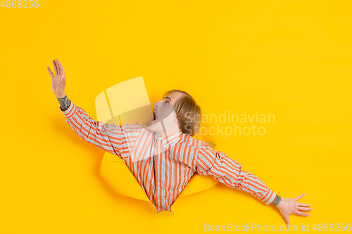 Image of Cheerful young man poses in torn yellow paper hole background, emotional and expressive