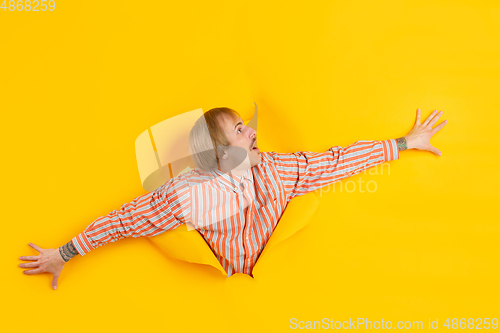 Image of Cheerful young man poses in torn yellow paper hole background, emotional and expressive