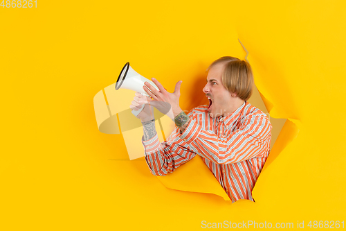 Image of Cheerful young man poses in torn yellow paper hole background, emotional and expressive