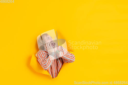 Image of Cheerful young man poses in torn yellow paper hole background, emotional and expressive