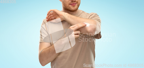 Image of young man applying pain medication to his elbow