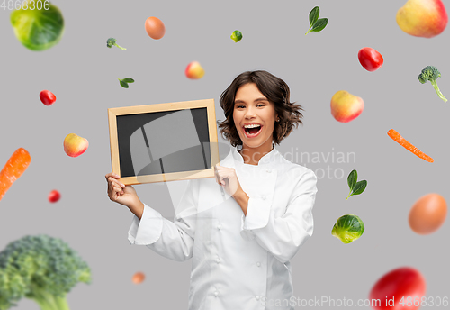 Image of happy female chef holding chalkboard over food