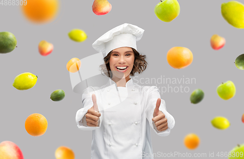 Image of happy female chef showing thumbs up over fruits