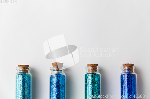 Image of blue glitters in bottles over white background