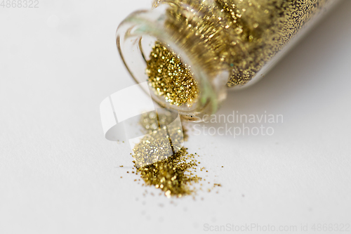 Image of golden glitters poured from small glass bottle