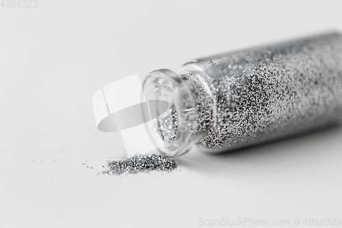 Image of silver glitters poured from small glass bottle