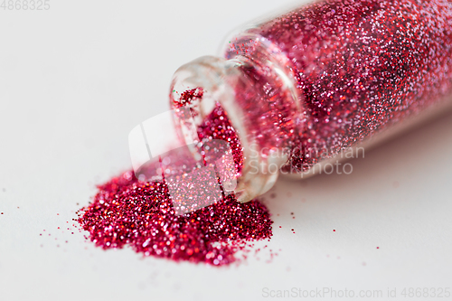 Image of pink red glitters poured from small glass bottle