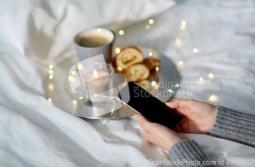 Image of hands with smartphone, croissant and coffee in bed