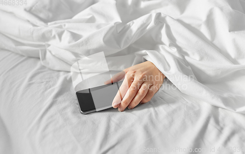 Image of hand of woman lying in bed with smartphone